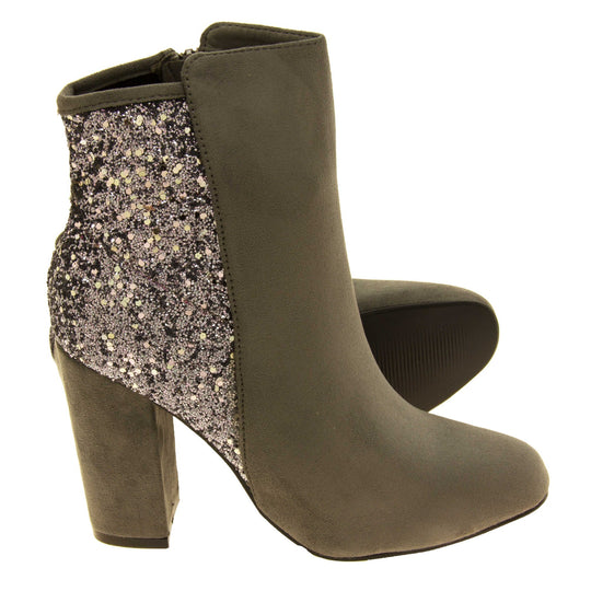 Suede ankle boots women. Grey faux suede upper with the back half of the boot covered in silver glitter. Zip fastening down the inside leg of the boot. With a grey block high heel and black sole. Both feet from a side profile with the left foot on its side to show the sole.
