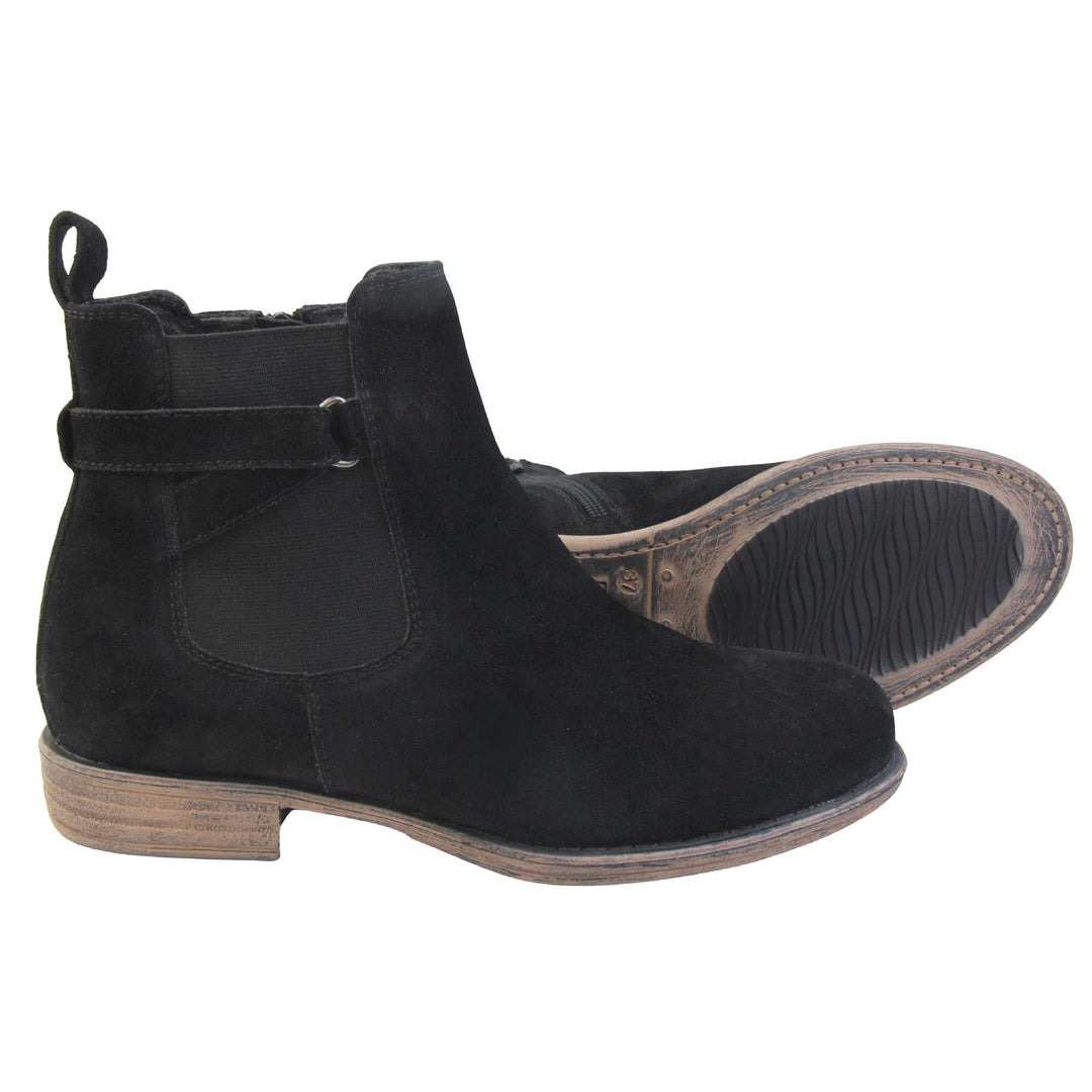 Suede leather ankle boots. Chelsea boot style with a black suede upper. Black elasticated panels at the ankles with straps in a zigzag across the panel. Black loop at the back to help pull them on. Brown sole with a slight heel. Both feet from a side profile with the left foot on its side to show the sole.