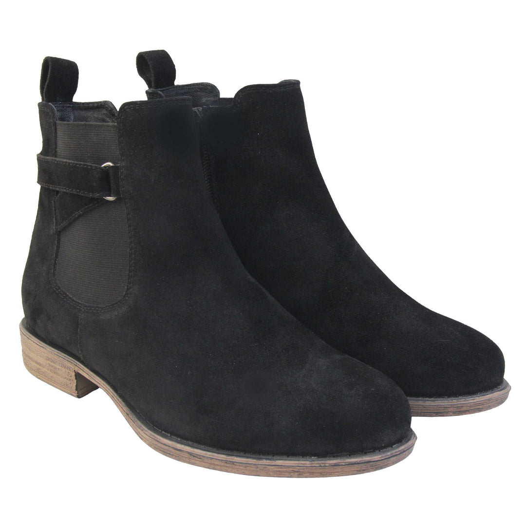 Suede leather ankle boots. Chelsea boot style with a black suede upper. Black elasticated panels at the ankles with straps in a zigzag across the panel. Black loop at the back to help pull them on. Brown sole with a slight heel. Both feet together from an angle.