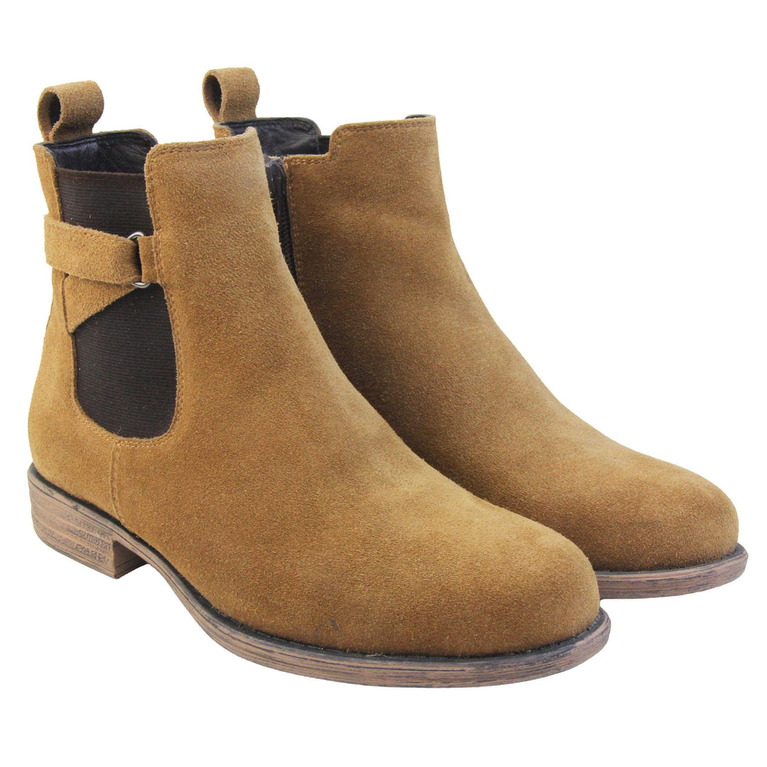 Suede leather Chelsea boots. Women's ankle boot with a tan suede upper. Black elasticated panels at the ankles with straps in a zigzag across the panel. Brown loop at the back to help pull them on. Brown sole with a slight heel. Both feet together from an angle. Both feet together from an angle.