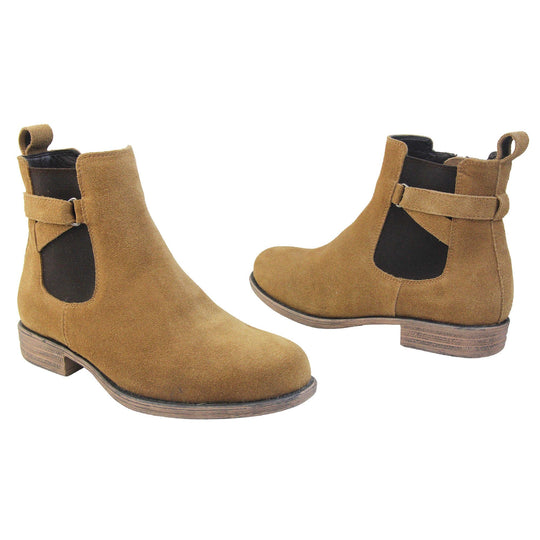 Suede leather Chelsea boots. Women's ankle boot with a tan suede upper. Black elasticated panels at the ankles with straps in a zigzag across the panel. Brown loop at the back to help pull them on. Brown sole with a slight heel. Both feet from a slight angle facing top to tail.