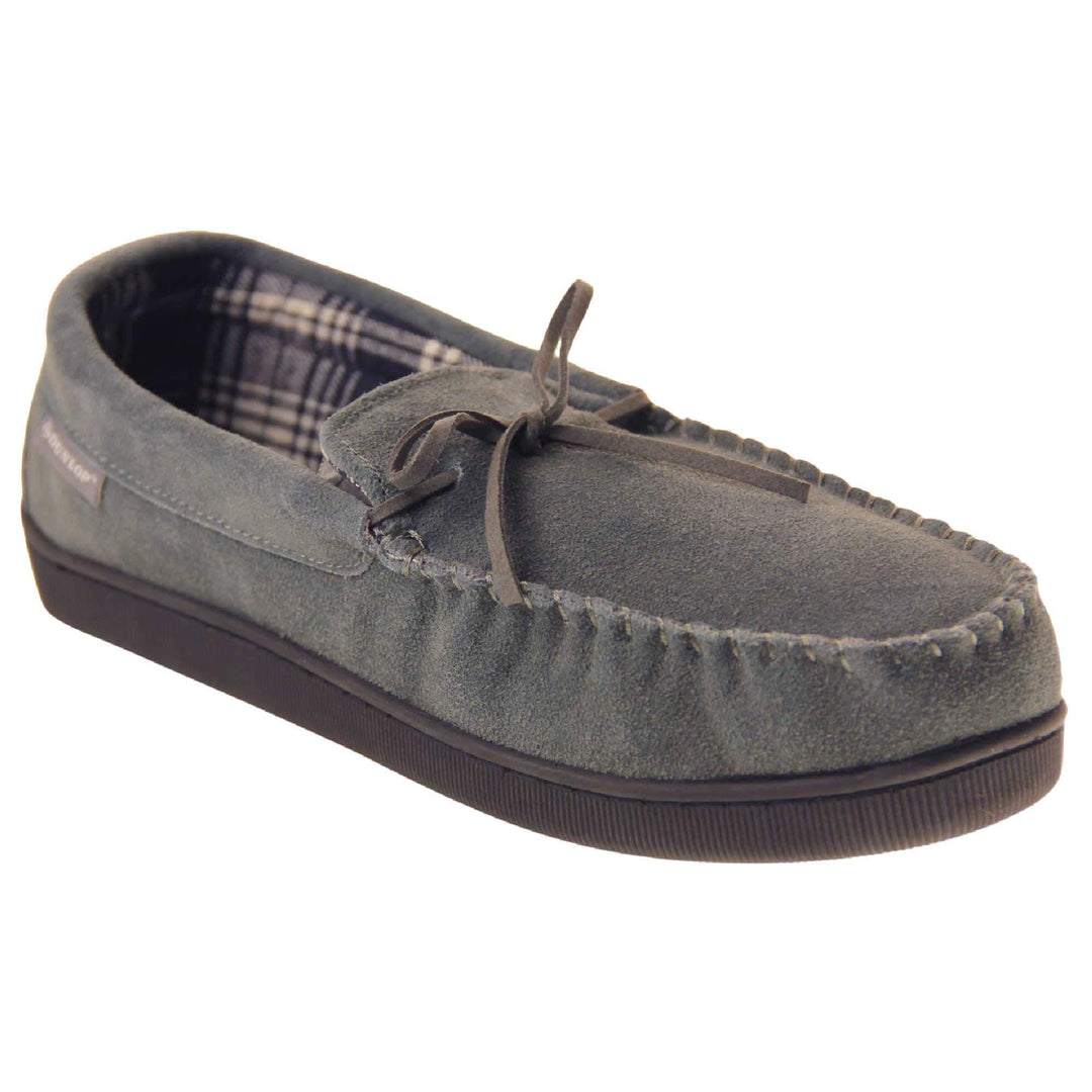 Suede moccasin slippers. Moccasin style slipper with grey suede upper and leather bow to the top. Grey Dunlop label to the outside. Grey and white plaid textile lining. Black rubber sole. Right foot at an angle.