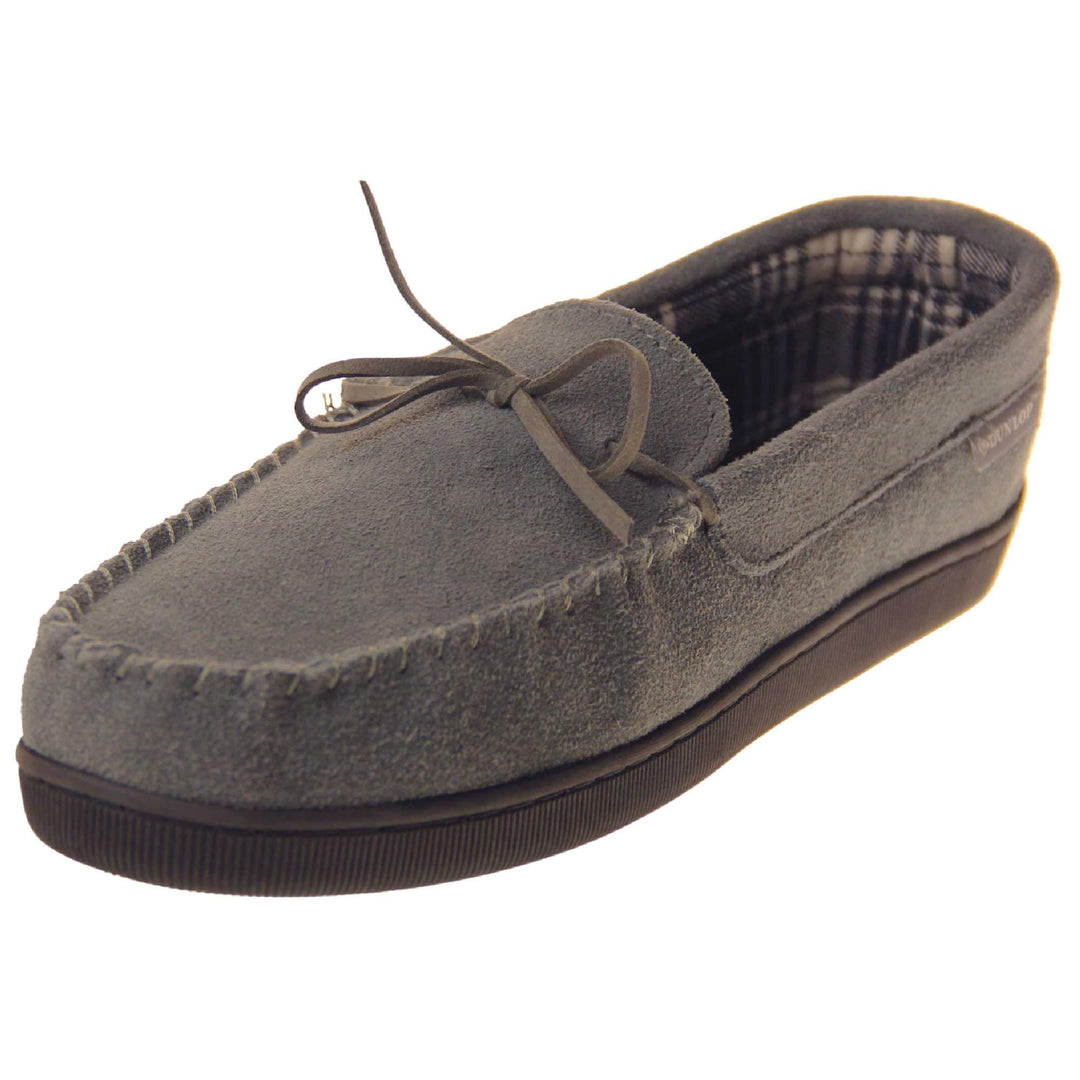 Suede moccasin slippers. Moccasin style slipper with grey suede upper and leather bow to the top. Grey Dunlop label to the outside. Grey and white plaid textile lining. Black rubber sole. Left foot at an angle.