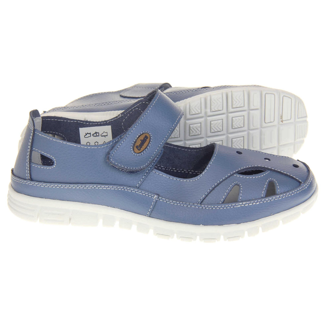 Comfy wide fit sandals. Mary Jane style shoes. Blue leather uppers with white stitching detail. Blue touch fasten strap over the foot with brown oval with Coolers branding on. Cut outs in the middle, edges and heel of the shoes. White sole with grip to the bottom. Both feet from a side profile with left foot on its side behind the right to show the sole.