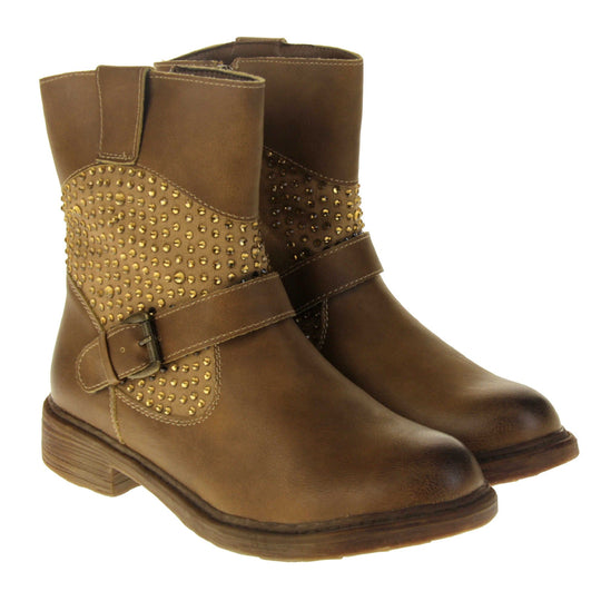 Tan flat ankle boots women. Biker style ankle boot with a tan faux leather upper. Textile panel running around the ankle with gold diamante studs covering it. Single strap with buckle over the top of the ankle. Zip fastening down the inside of the boot. Brown sole with a slight heel. Both feet together from an angle.