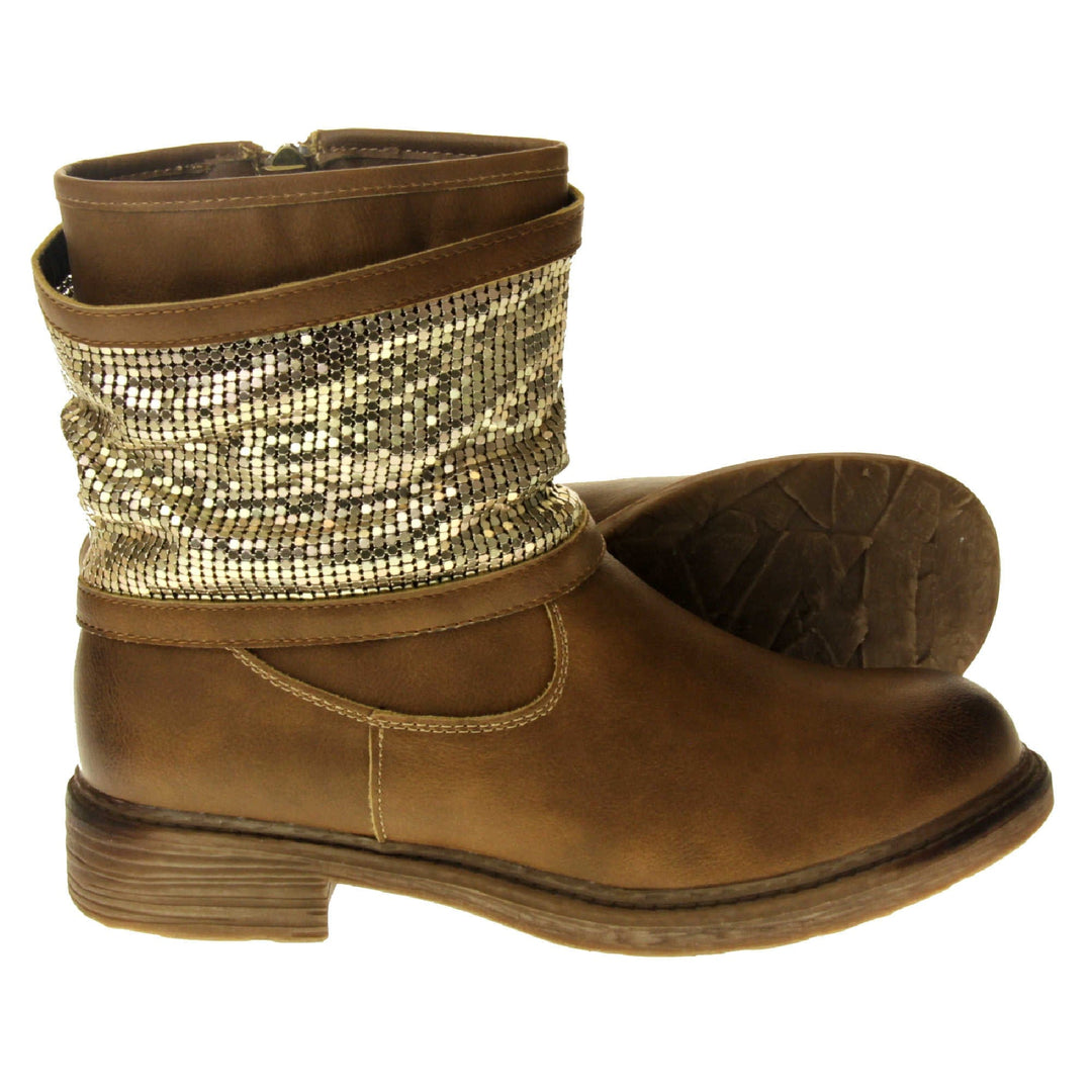 Tan sparkle ankle boots women. Biker style ankle boot with a tan faux leather upper. A thick band of shiny gold chainmail runs around the ankle. Zip fastening down the inside of the boot. Brown sole with a slight heel.  Both feet from a side profile with the left foot on its side to show the sole.