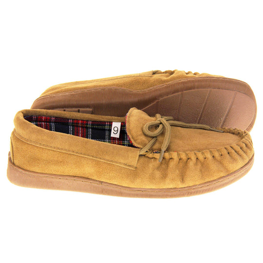 Tartan slippers. Moccasin style slipper with tan suede upper and leather bow to the top. Blue and red tartan plaid lining. Beige synthetic sole. Both feet from a side profile with the left foot on its side to show the sole.