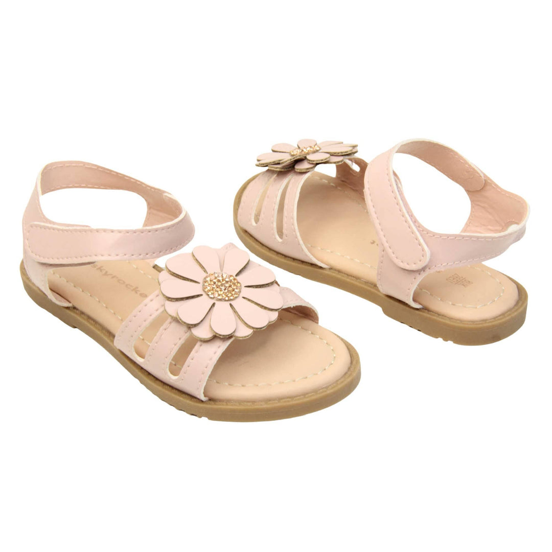 Toddler shoes girl. Strappy sandals with pale pink faux leather strappy upper. With around the ankle strap with hook and loop fastening. Pink flower detailing to the front of the shoe with a diamante middle. Beige coloured insole with Skyrocket branding in brown. Brown sole with grip to the bottom. Both feet at an angle facing top to tail.
