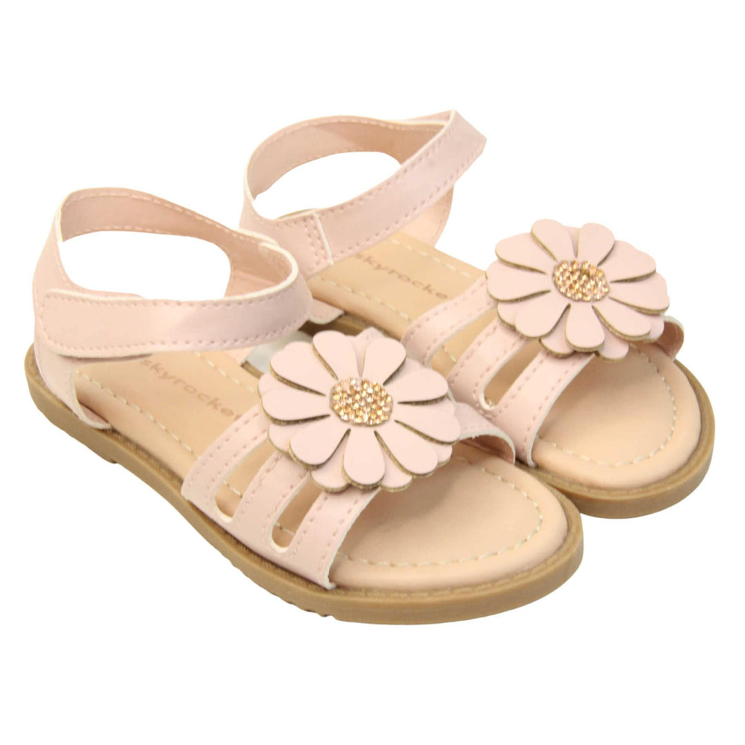 Toddler shoes girl. Strappy sandals with pale pink faux leather strappy upper. With around the ankle strap with hook and loop fastening. Pink flower detailing to the front of the shoe with a diamante middle. Beige coloured insole with Skyrocket branding in brown. Brown sole with grip to the bottom. Both feet together at an angle.