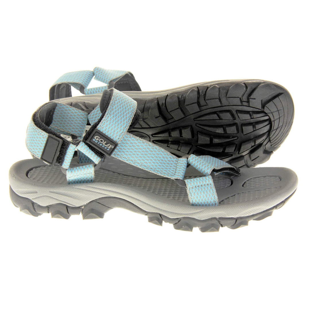 Walking sandals women. Womens sporty style sandals. Grey textile straps with blue criss-cross pattern. Black padding to the heel and over foot strap. Touch fasten strap around the heel. Black Gola branding to the ankle of the sandal. Grey textile lining and black sole with chunky grip to the base. Both feet from a side profile with the left foot on its side behind the the right foot to show the sole.