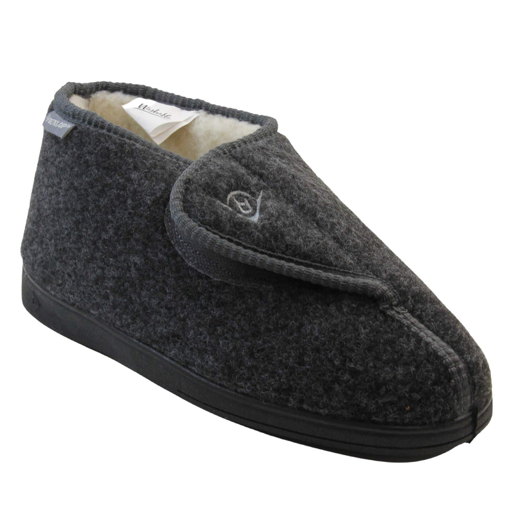 Orthopaedic slippers. Mens orthopaedic slippers in an ankle boot style. With a grey felt upper and white fleece lining. With an adjustable touch close top with a grey Dunlop logo on. Small grey label to the outer side edge with Dunlop written on. Thick black outdoor sole. Right foot at an angle.