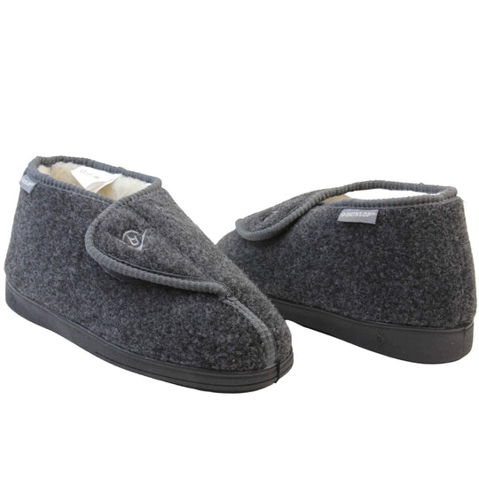 Orthopaedic slippers. Mens orthopaedic slippers in an ankle boot style. With a grey felt upper and white fleece lining. With an adjustable touch close top with a grey Dunlop logo on. Small grey label to the outer side edge with Dunlop written on. Thick black outdoor sole.  Both feet at a slight angle facing top to tail.
