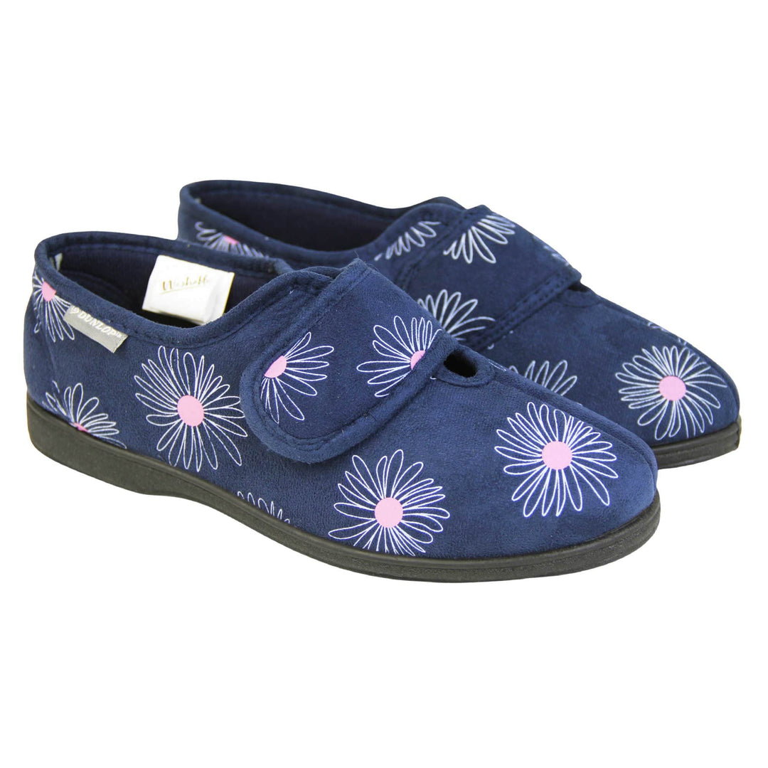Washable slippers womens. Ladies full back slipper. Navy blue upper with white daisy design and bright pink for the middle of the flowers. Touch fasten strap over the top of the foot to adjust the fit. Matching blue textile lining and sole. Both feet together at angle.