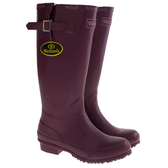Womens Wellies. Purple rubber waterproof wellington boots. Just below knee height. With a small heel and deep tread to the sole. Pink Wetlands Brand to the front of the boot near the top. Wetlands written in Lilac numerous times around the rim of the boot. Side strap with buckle to adjust the calf width. Textile lining to the inside of the boot. Both boots next to each other