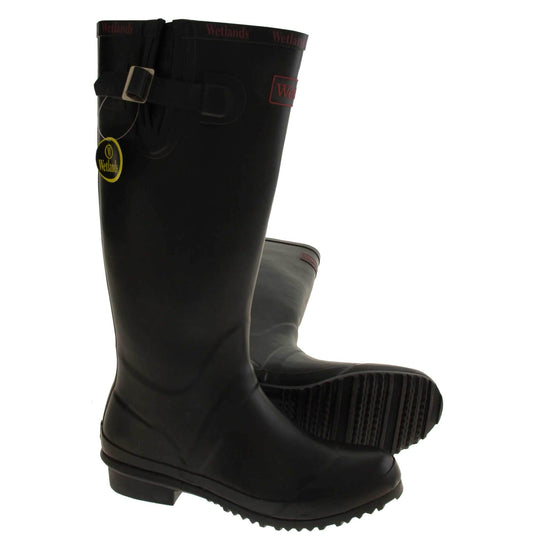 Womens Wellies. Black rubber waterproof wellington boots. Just below knee height. With a small heel and deep tread to the sole. Red Wetlands Brand to the front of the boot near the top. Wetlands written in red numerous times around the rim of the boot. Side strap with buckle to adjust the calf width. Textile lining to the inside of the boot. Both feet from a side profile but with the left foot on it side to show you the sole.