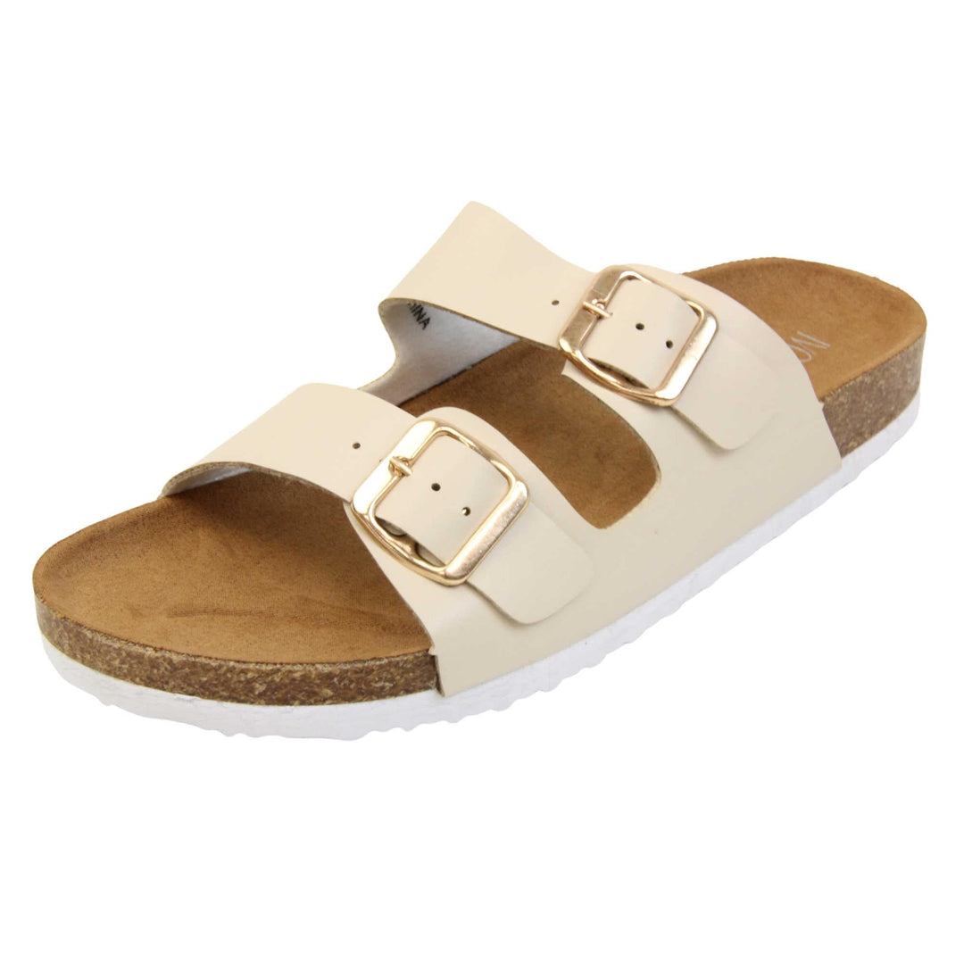 White double strap sandals. Womens dual strap slip on sandals. With a white synthetic leather upper with a gold buckle on each strap. Brown faux suede insole with a moulded footbed. Cork effect outsole with white base with grip to the bottom. Left foot at an angle.