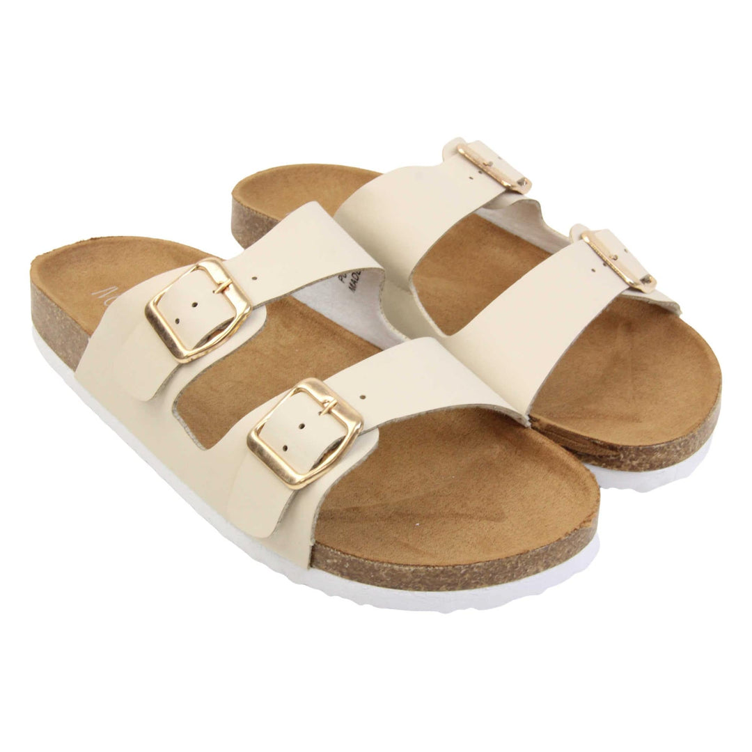 White double strap sandals. Womens dual strap slip on sandals. With a white synthetic leather upper with a gold buckle on each strap. Brown faux suede insole with a moulded footbed. Cork effect outsole with white base with grip to the bottom. Both feet together at a slight angle.