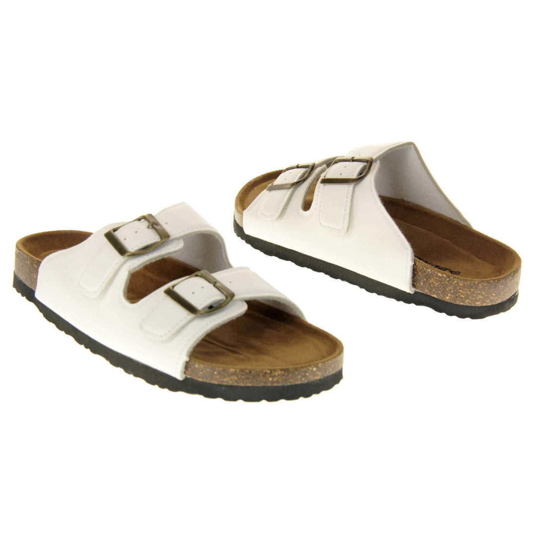 White flat sandals womens. Ladies dual strap slip on sandals. With a white synthetic leather upper with a gold buckle on each strap. Brown faux suede insole with a moulded footbed. Cork effect outsole with black base with grip to the bottom. Both feet at an angle facing top to tail.