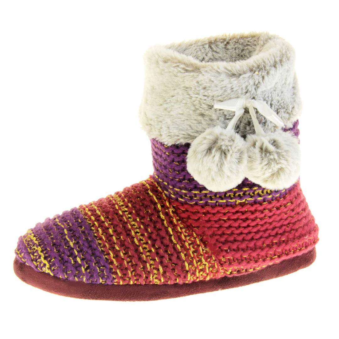 Womens knit slippers. Boot style slippers in a knit upper. Plum fading purple ombre effect with gold thread detailing. Light grey faux fur collar and lining with matching pom poms to the side. Left foot at an angle.