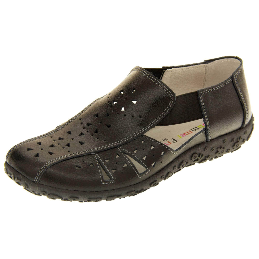 Womens black sandals. Black leather closed toe sandals with white stitched detailing. With small cut out details on the upper. Black elasticated strips from tongue to ankle to allow more room for a better fit. Cream coloured leather insole and lining. Black sole with heel having a slight platform with raised flower design for grip. Left foot at an angle.