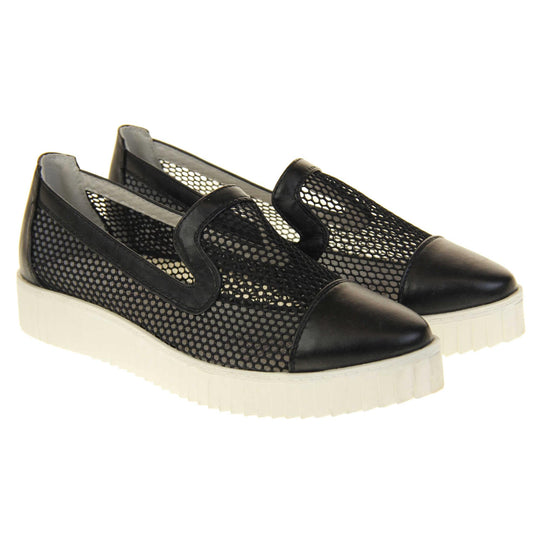 Womens flatforms. Loafer style shoes with a black net upper and black faux leather toe, heel and collar. White flat chunky platform. Cream insole. Both feet together at a slight angle.