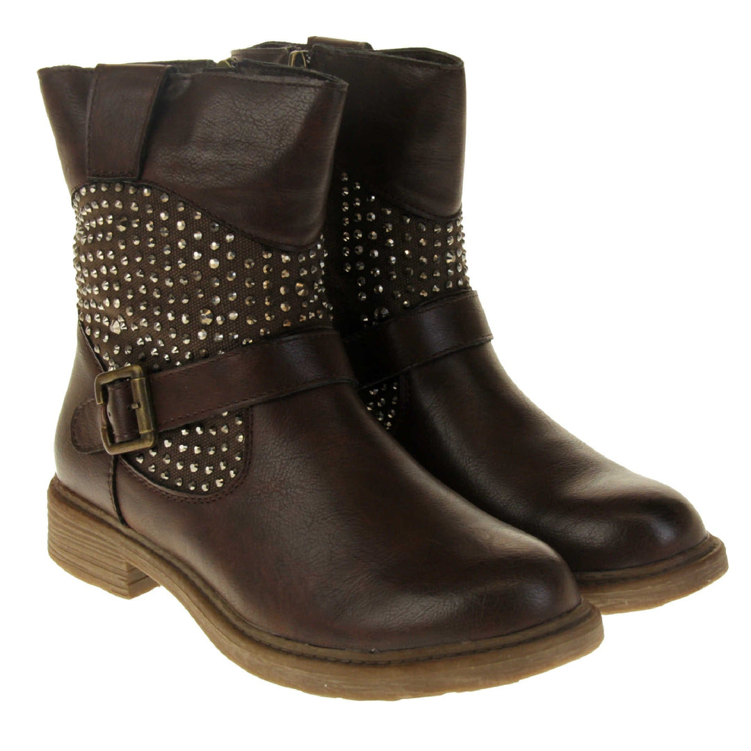 Womens leather biker boots. Biker style ankle boot with a brown faux leather upper. Textile panel running around the ankle with dark bronze diamante studs covering it. Single strap with buckle over the top of the ankle. Zip fastening down the inside of the boot. Brown sole with a slight heel. Both feet together from an angle.