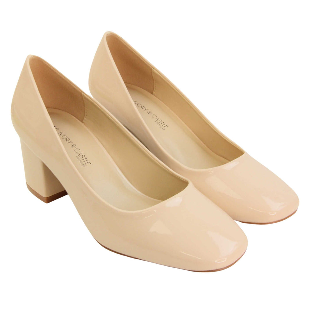 Womens nude block heel. Womens court shoes with nude patent faux leather uppers. Nude block heel. Beige faux leather lining with beige textile lining at the heel. Beige sole. Both feet together at an angle.