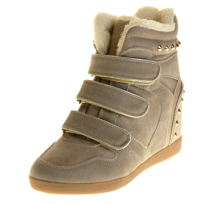 Women's wedge ankle boot. Ankle boot in a sneaker style with a grey faux suede upper. Wedge heel is hidden so the boots look flat. Three touch fasten straps across the front for fastening. Cream faux fur lining and trim. Gold studs around the collar and heel. Beige sole with good grip to the bottom. Left foot at an angle.
