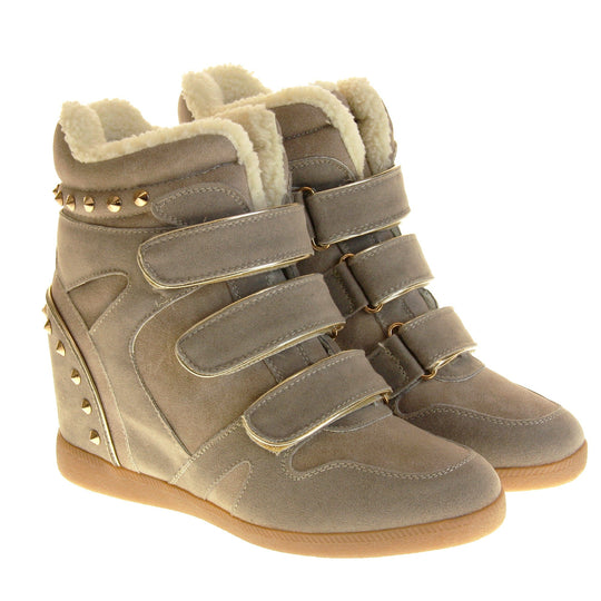 Women's wedge ankle boot. Ankle boot in a sneaker style with a grey faux suede upper. Wedge heel is hidden so the boots look flat. Three touch fasten straps across the front for fastening. Cream faux fur lining and trim. Gold studs around the collar and heel. Beige sole with good grip to the bottom. Both feet together from an angle.