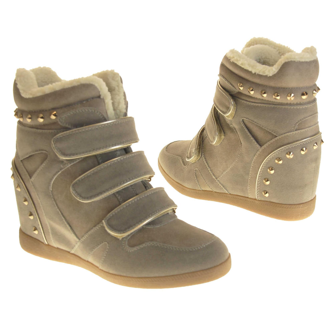 Women's wedge ankle boot. Ankle boot in a sneaker style with a grey faux suede upper. Wedge heel is hidden so the boots look flat. Three touch fasten straps across the front for fastening. Cream faux fur lining and trim. Gold studs around the collar and heel. Beige sole with good grip to the bottom. Both feet from a slight angle facing top to tail.