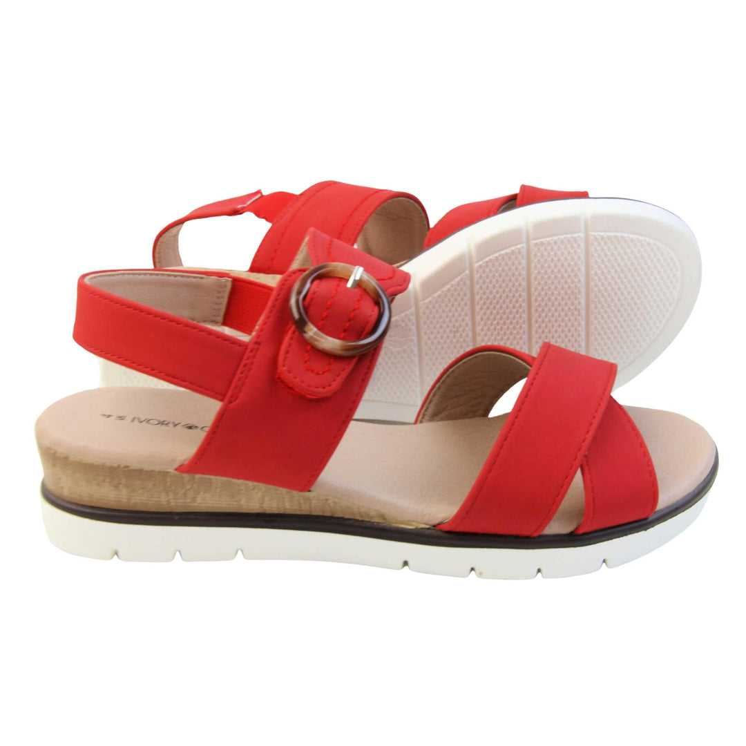 Womens wedge sandals. Classic womens strappy sandals with red textile straps. Dual toe straps that cross over each other. The ankle strap is touch fasten but has a brown buckle detail to look like a buckle fastening. Beige faux leather memory foam insoles. Small wedge heel in cork effect. White outsole with a black rim around the top. Both feet from a side profile with left foot on its side behind the right to show the sole.