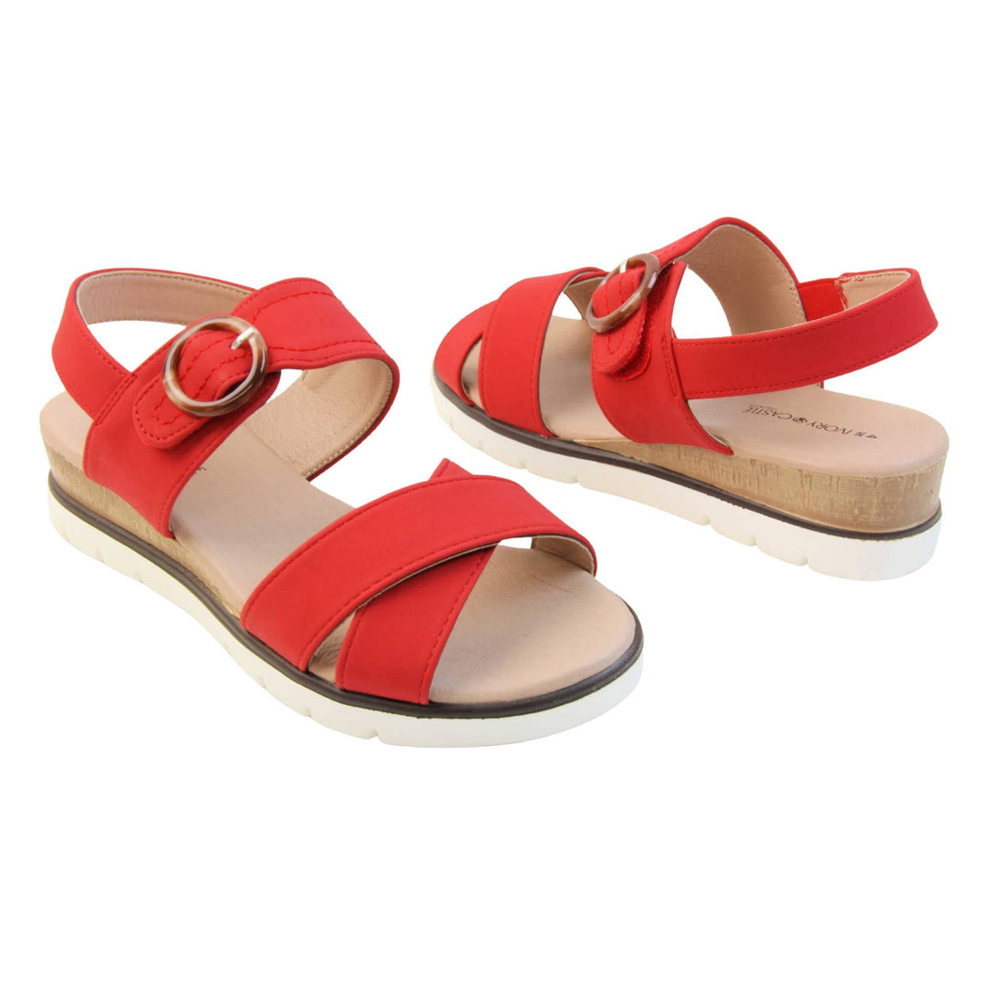 Womens wedge sandals. Classic womens strappy sandals with red textile straps. Dual toe straps that cross over each other. The ankle strap is touch fasten but has a brown buckle detail to look like a buckle fastening. Beige faux leather memory foam insoles. Small wedge heel in cork effect. White outsole with a black rim around the top. Both shoes about an inch apart at a slight angle facing top to tail.