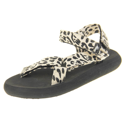 Womens adjustable sandals. Black foam platform outsole with cream canvas straps patterned with black dots to look similar to leopard print. Three adjustable touch fasten straps. Around the front and back of the ankle and one around the toes. Left foot at an angle.