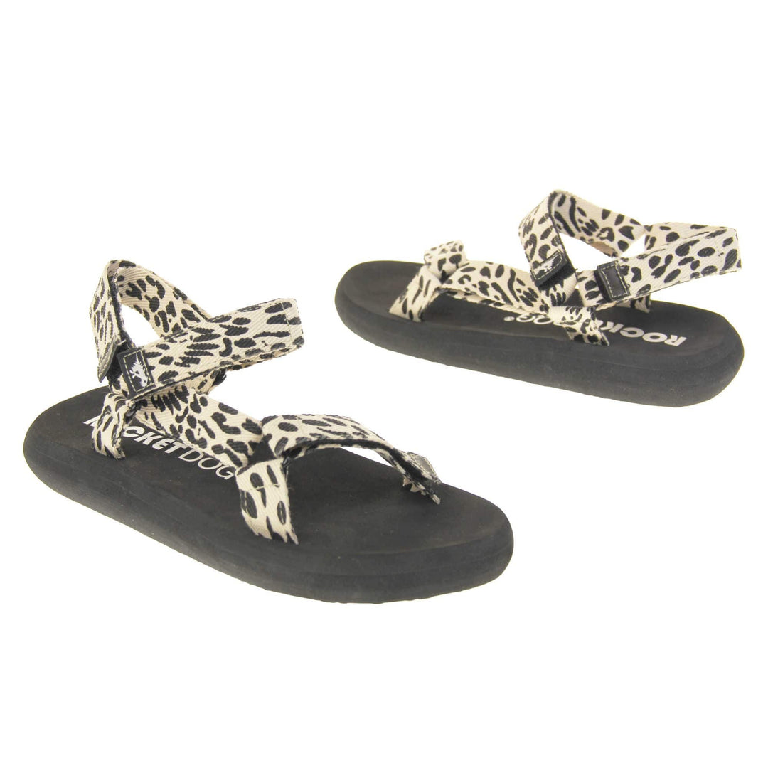 Womens adjustable sandals. Black foam platform outsole with cream canvas straps patterned with black dots to look similar to leopard print. Three adjustable touch fasten straps. Around the front and back of the ankle and one around the toes. Both feet facing opposite directions.