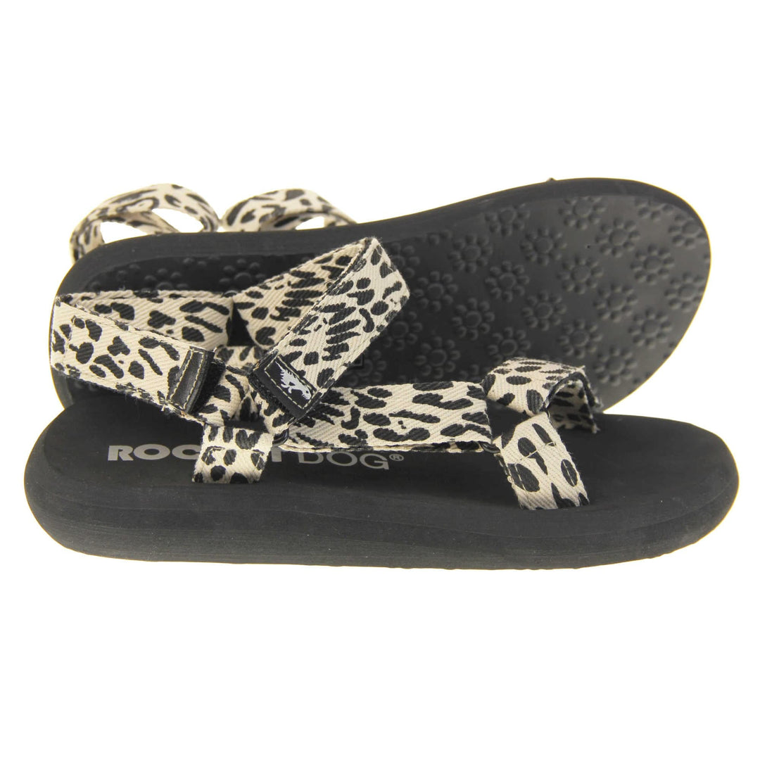 Womens adjustable sandals. Black foam platform outsole with cream canvas straps patterned with black dots to look similar to leopard print. Three adjustable touch fasten straps. Around the front and back of the ankle and one around the toes. Right foot side on with left foot outsole showing.