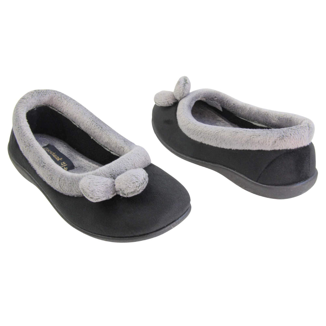 Womens ballerina slippers. Womens ballerina style slippers with black velour uppers. Grey, plush textile collar and two pom poms to the front of the shoe. Matching textile lining. Firm black sole. Both feet at an angle facing top to tail.