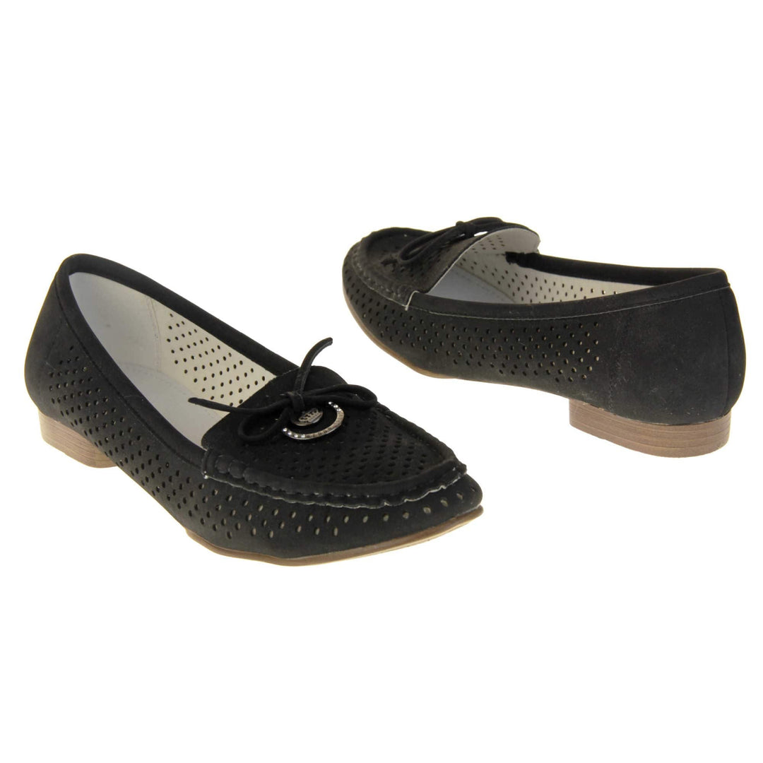 Womens black boat shoes. loafer style shoes with a black faux suede upper. Cut out dots along the sides and top of the shoe. Bow detail with metal hoop to the tongue of the shoe. Cream lining. Brown sole with slight heel. Both feet at an angle facing top to tail.