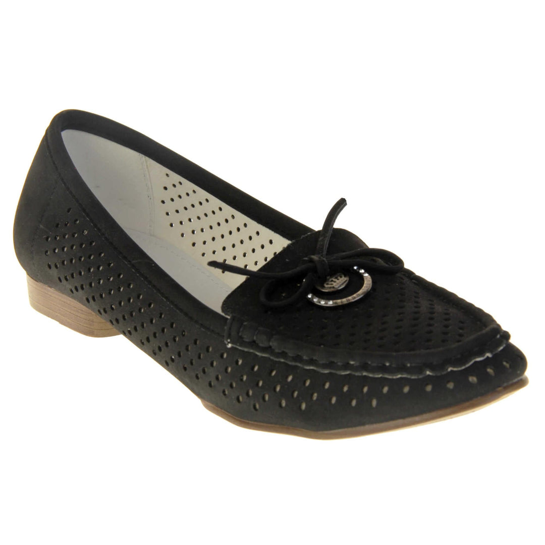 Womens black boat shoes. loafer style shoes with a black faux suede upper. Cut out dots along the sides and top of the shoe. Bow detail with metal hoop to the tongue of the shoe. Cream lining. Brown sole with slight heel. Right foot at an angle.