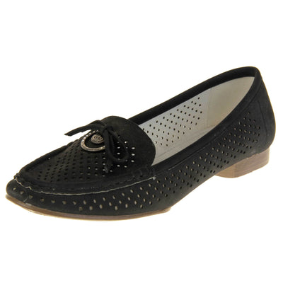 Womens black boat shoes. loafer style shoes with a black faux suede upper. Cut out dots along the sides and top of the shoe. Bow detail with metal hoop to the tongue of the shoe. Cream lining. Brown sole with slight heel. Left foot at an angle.