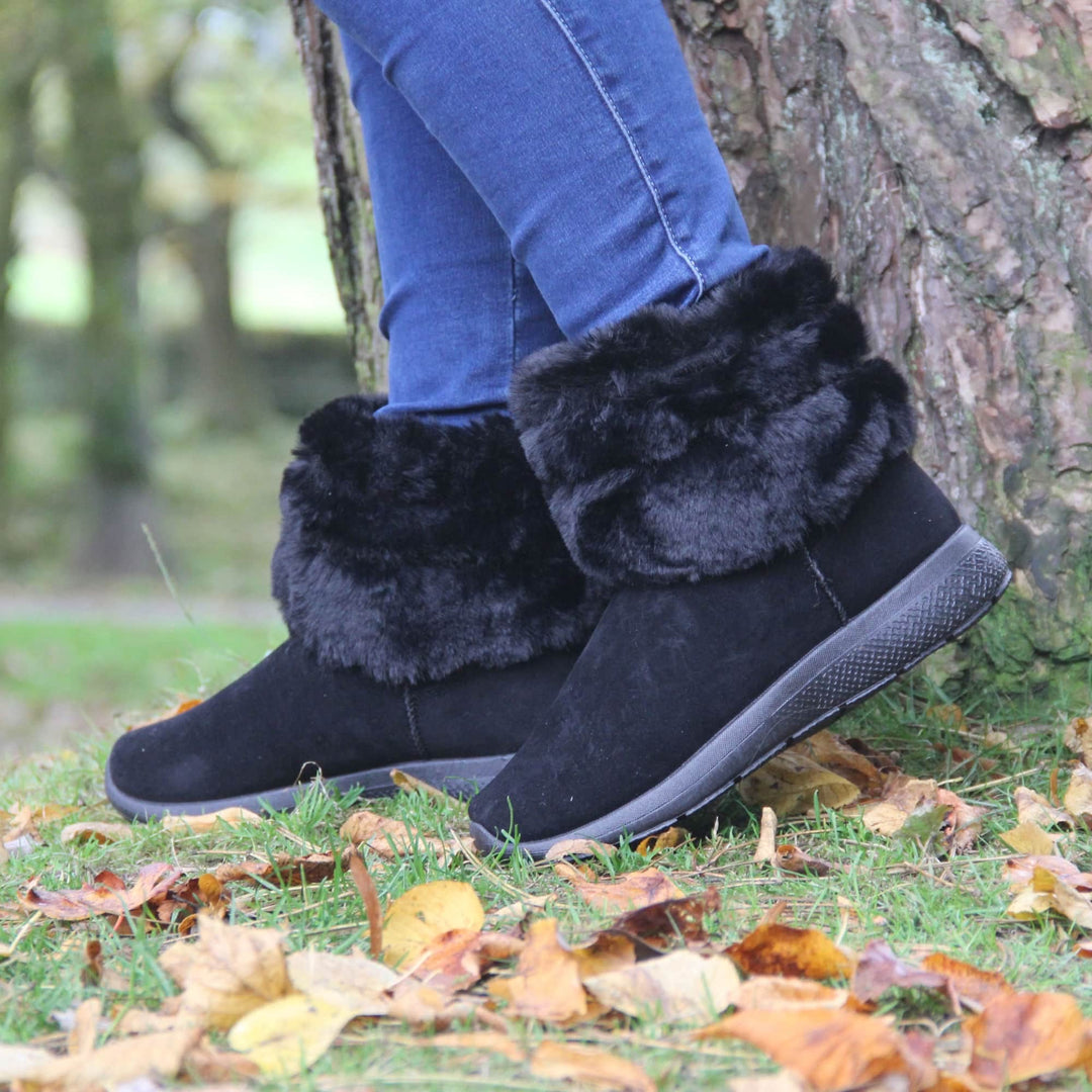 Womens Faux Fur Lined Ankle Boots - Black ankle boots with slight wedge heel, suede effect upper with soft faux fur cuff, scuff resistant bumper to front. Model shot in Autumn in park.