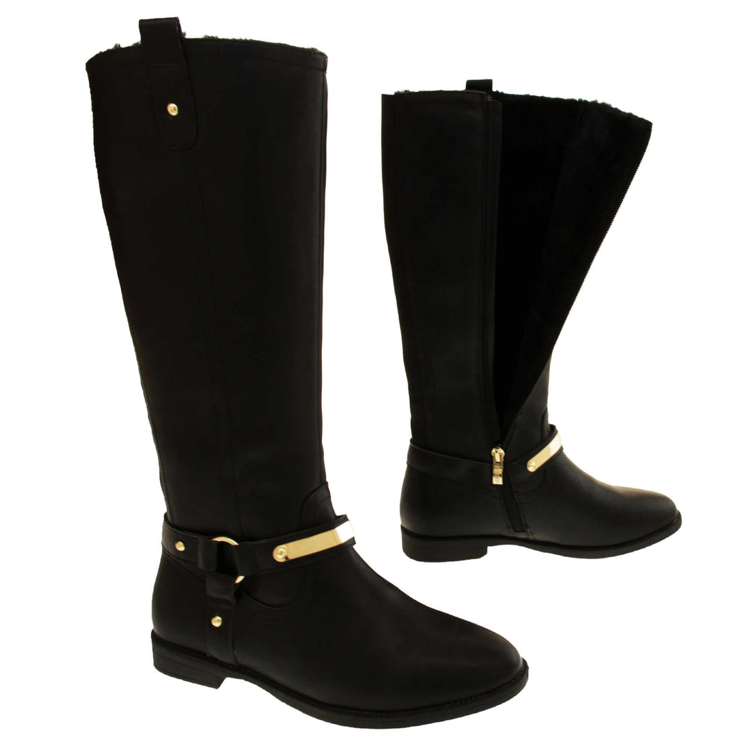 Womens black leather knee high boots. Knee high style boots with a black faux leather upper. A Tri strap going around the ankle and down to the bottom of the boot joined by the ankle with a good loop. Gold plate to the front of the ankle strap. Zip up the inside of the boot. Faux leather loop on the top of the outside of the boot to help with pulling it on. Both feet about a foot apart from the side. Left foot showing the inside of the boot unzipped and the faux fur lining.
