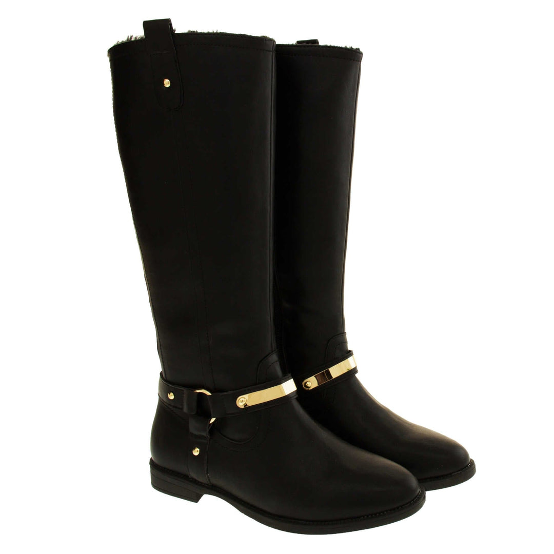 Womens black leather knee high boots. Knee high style boots with a black faux leather upper. A Tri strap going around the ankle and down to the bottom of the boot joined by the ankle with a good loop. Gold plate to the front of the ankle strap. Zip up the inside of the boot. Faux leather loop on the top of the outside of the boot to help with pulling it on. Both shoes together at an angle.