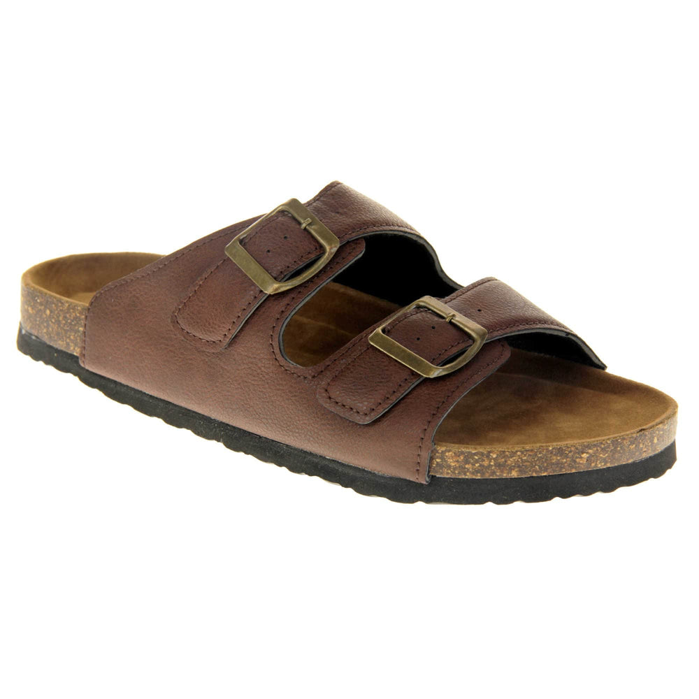 Womens brown slide sandals. Ladies dual strap slip on sandals. With a brown synthetic leather upper with a gold buckle on each strap. Brown faux suede insole with a moulded footbed. Cork effect outsole with black base with grip to the bottom. Right foot at an angle.