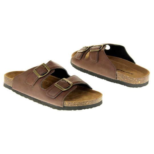 Womens brown slide sandals. Ladies dual strap slip on sandals. With a brown synthetic leather upper with a gold buckle on each strap. Brown faux suede insole with a moulded footbed. Cork effect outsole with black base with grip to the bottom. Both feet at an angle facing top to tail.