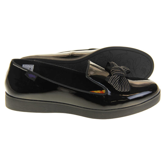 Women's comfortable loafers. Loafer style shoes with a black faux patent leather upper. With a black bow detail on the top of the foot. Bright floral patterned insole. Chunky black sole with slip resistant grip to the bottom. Both feet from a side profile with the left foot on its side behind the the right foot to show the sole.