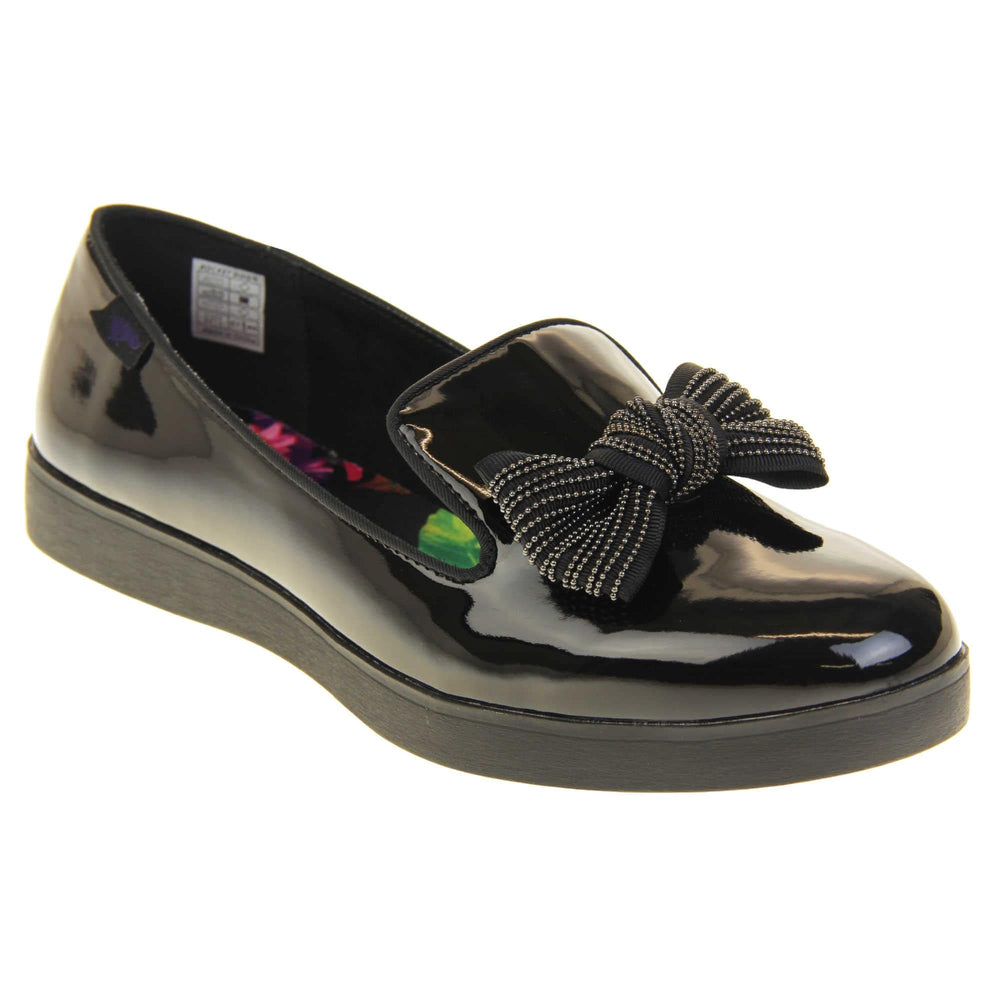 Women's comfortable loafers. Loafer style shoes with a black faux patent leather upper. With a black bow detail on the top of the foot. Bright floral patterned insole. Chunky black sole with slip resistant grip to the bottom. Right foot at an angle.