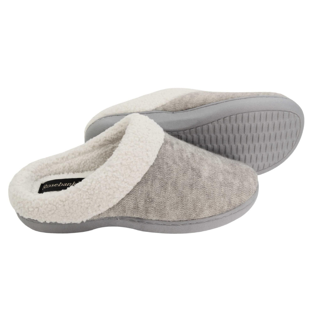 Womens cotton slippers. Womens slippers in a mule style. With grey cotton knit uppers and cream faux fur collar and lining. Grey hard synthetic soles with grip to the base. Both feet from a side profile with the left foot on its side to show the sole.