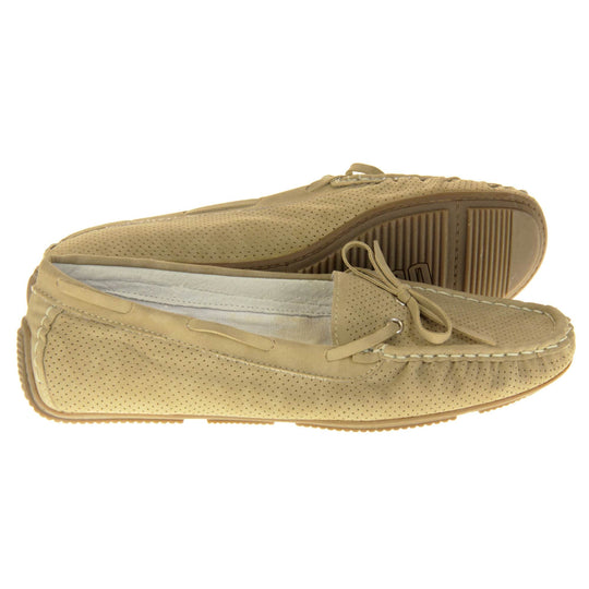Women's deck shoes. Loafer style boat shoes with a beige faux leather upper and tiny dot cut-outs. Beige lace detail running around the outside of the collar. White stitching detailing around the top of the shoe. Cream leather lining and beige sole. Both feet from a side profile with the left foot on its side behind the the right foot to show the sole.