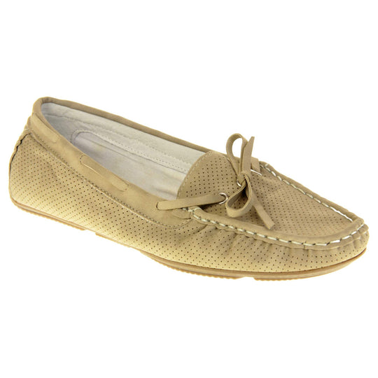 Women's deck shoes. Loafer style boat shoes with a beige faux leather upper and tiny dot cut-outs. Beige lace detail running around the outside of the collar. White stitching detailing around the top of the shoe. Cream leather lining and beige sole. Right foot at an angle.