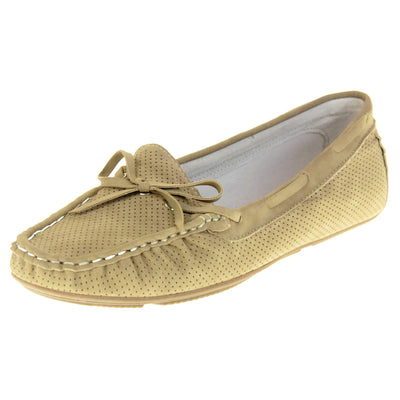 Women's deck shoes. Loafer style boat shoes with a beige faux leather upper and tiny dot cut-outs. Beige lace detail running around the outside of the collar. White stitching detailing around the top of the shoe. Cream leather lining and beige sole. Left foot at an angle.
